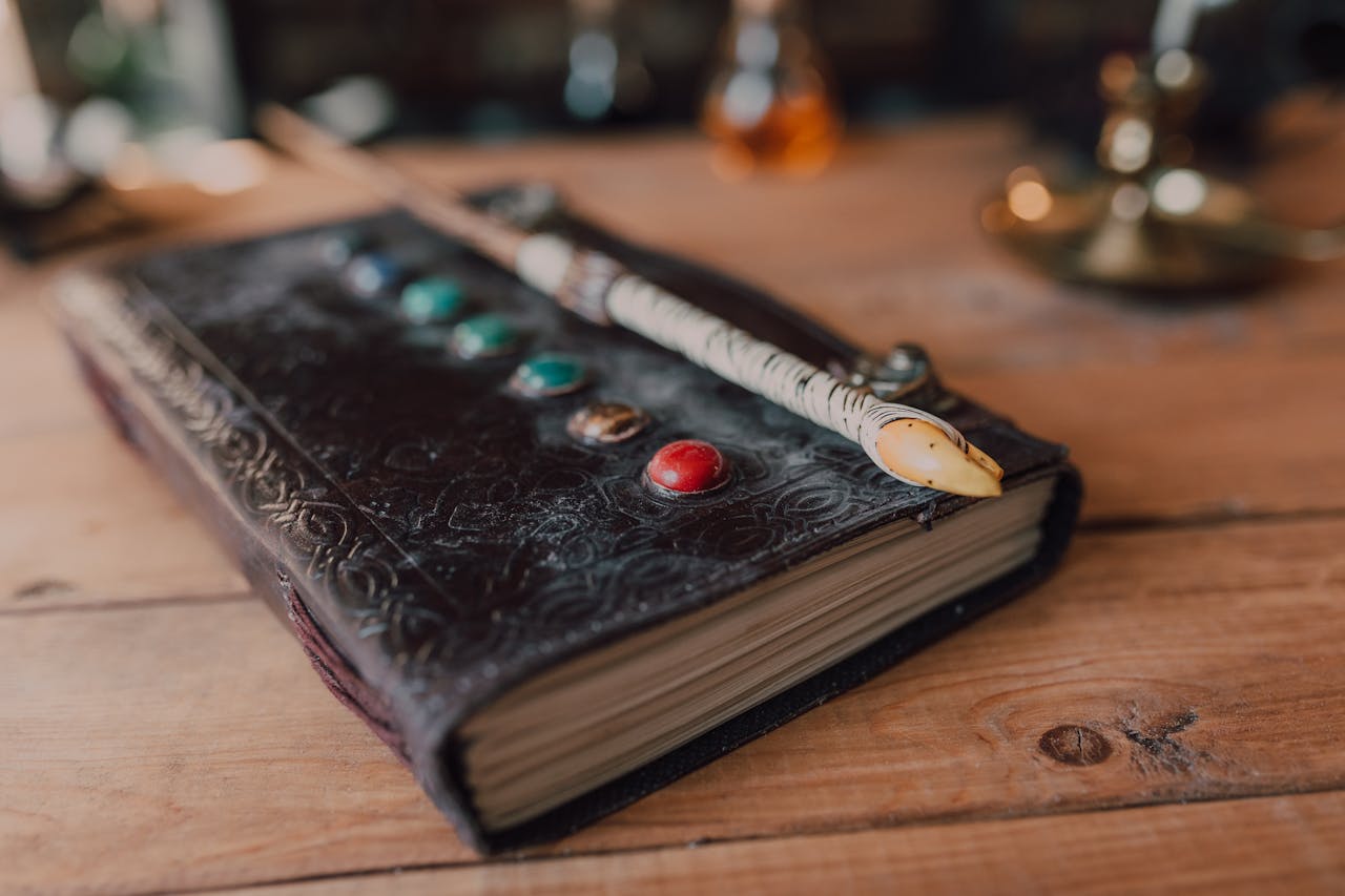 Close-up of a mystical spell book adorned with magical stones and a wand on wooden surface.